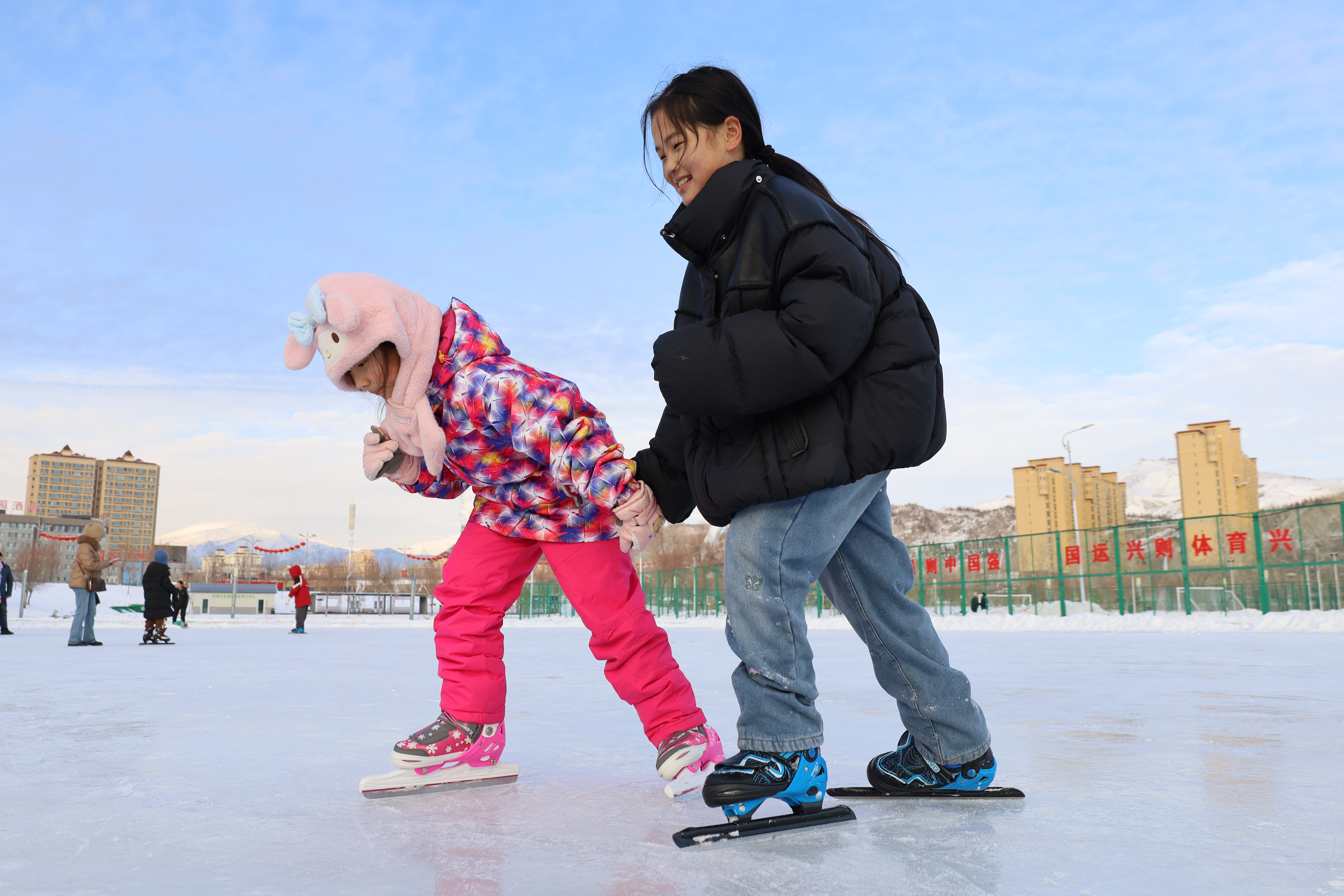 在滑冰场内，小朋友们手拉手滑冰，尽享冰雪运动的欢乐。